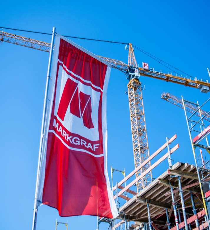 Markgraf-Fahne vor Baukran und Gerüst auf einer Baustelle bei blauem Himmel
